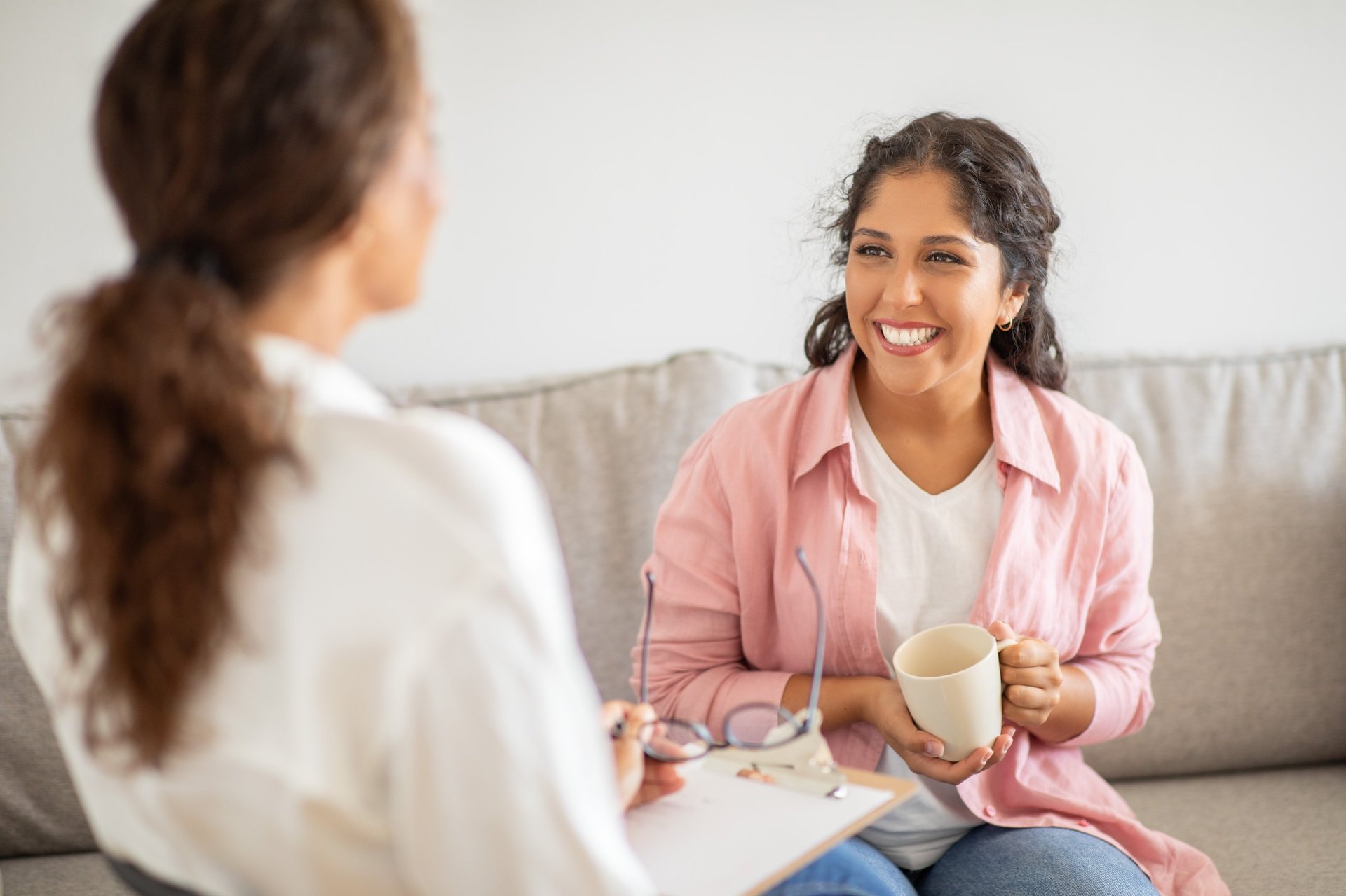Woman sitting on couch smiling while holding coffee